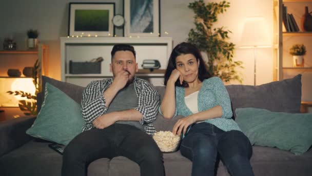 Manžel a manželka se dívají na televizi doma a jedí popcorn spolu pozdě v noci. — Stock video