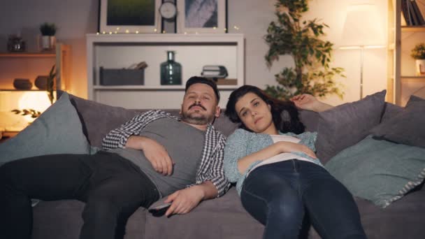 Pasangan mengantuk menonton TV di rumah larut malam menguap berbaring di sofa bersama-sama — Stok Video