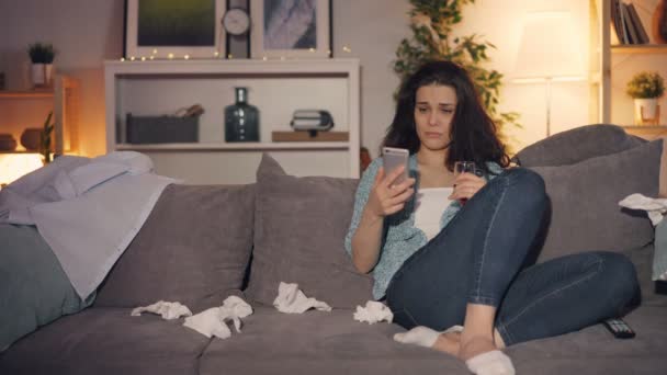 Δυστυχισμένη νεαρή γυναίκα κλάμα πίνοντας αλκοόλ χρησιμοποιώντας smartphone βλέποντας τηλεόραση στο σπίτι — Αρχείο Βίντεο
