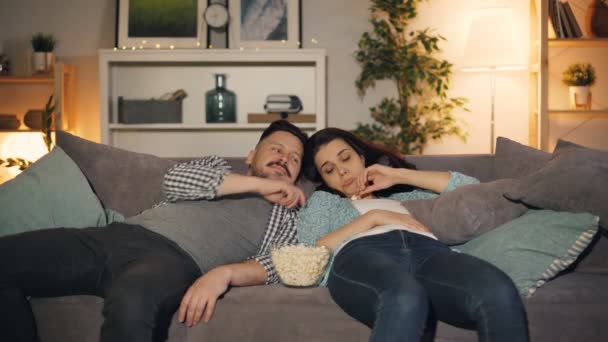 Feliz jovem casal assistindo show engraçado na TV rindo comer pipocas em casa — Vídeo de Stock
