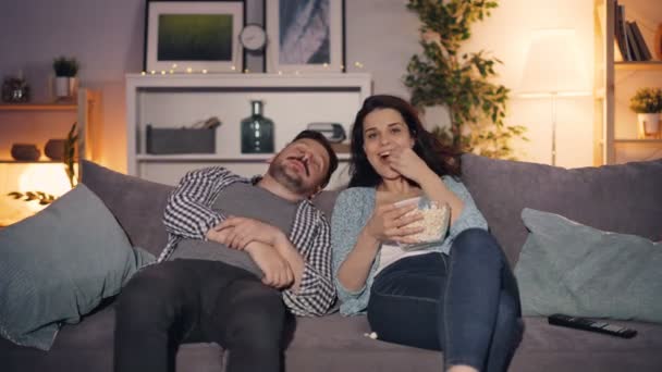 Чоловік приходить додому дивитися телевізор і розмовляє з дружиною їсть попкорн разом — стокове відео