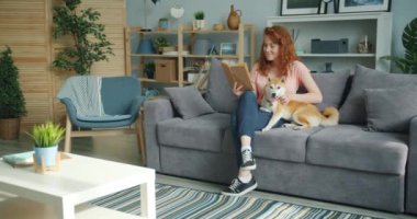 Çekici genç bayan ilginç kitap zevk ve evde sevimli köpek okşayarak