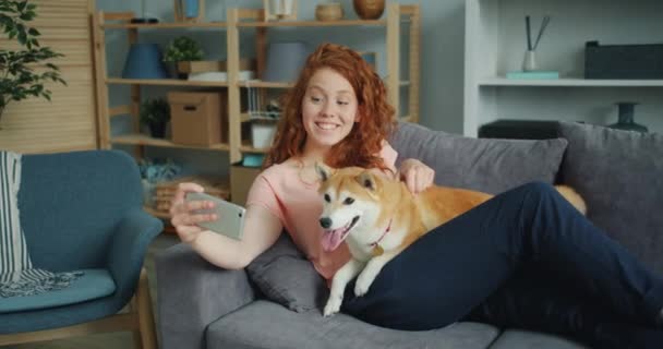 快乐的女孩采取silfie与可爱的狗使用智能手机相机在沙发上 — 图库视频影像
