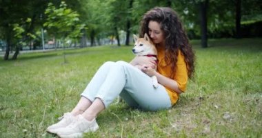 Parkta çimenlerin üzerinde oturan güzel shiba inu köpek okşayarak çekici esmer