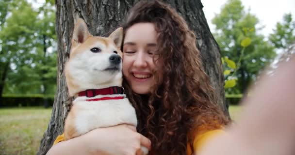 Retrato de menina feliz tomando selfie com cão no parque abraçando animal de estimação segurando câmera — Vídeo de Stock