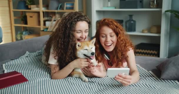 Happy Friends biorąc selfie z adorable Puppy leżącego na kanapie za pomocą smartfona — Wideo stockowe