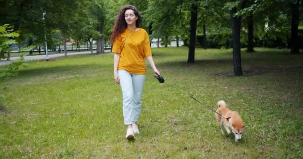 草の上に愛らしい柴犬と公園を歩く魅力的な若い女性 — ストック動画