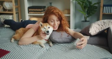 Sevimli köpek yavrusu öpüşme ve kanepede akıllı telefon ile selfie alarak Loving kadın