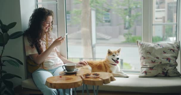 Pretty girl using smartphone stroking cute dog sitting on window sill in  cafe — Stock Video © silverkblack #284654536