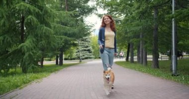 Yeşil parkta iyi yetişmiş köpek yavrusu yürüyen güzel kız yavaş hareket dolly çekim