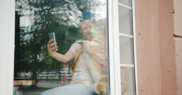 Studentin macht Selfie mit Hund mit Smartphone im Café auf Fensterbank — Stockvideo