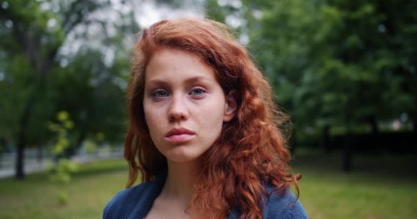 Zeitlupenporträt einer ziemlich seriösen Dame mit roten Haaren, die im Park steht — Stockvideo