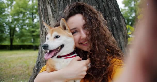 Retrato de dama atractiva tomando selfie con cachorro en parque besando abrazo perro — Vídeos de Stock