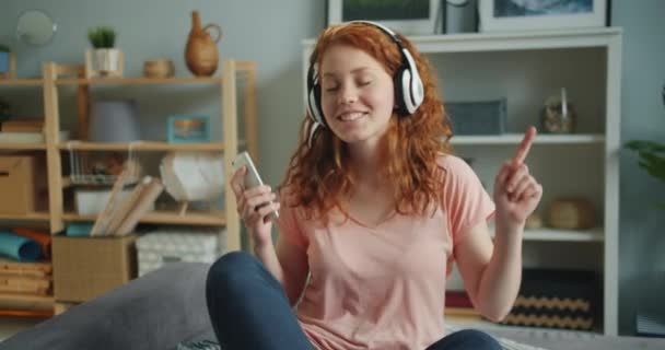 Alegre dama disfrutando de la música en los auriculares usando smartphone bailando en la cama — Vídeo de stock