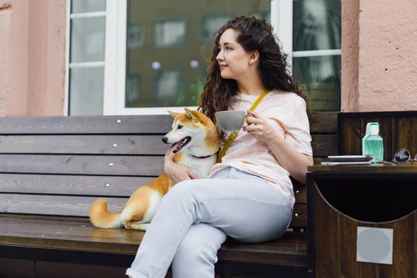 Chica bonita sentada en la cafetería de la calle con taza de té y shiba inu perro sonriendo —  Fotos de Stock