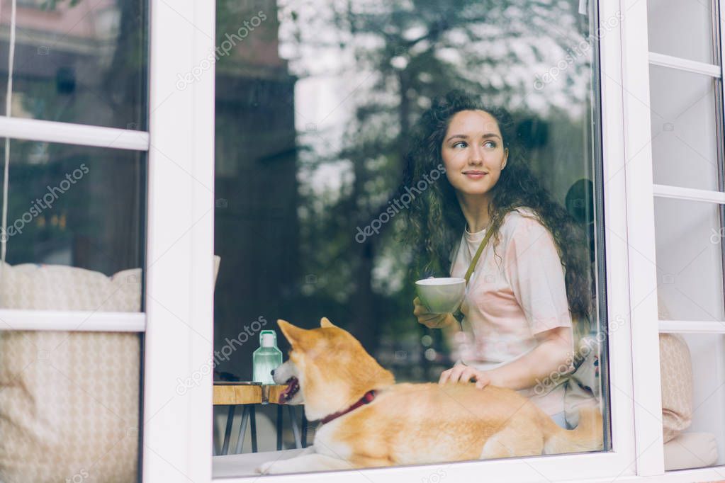 Cute girl relaxing in cafe with cup of coffee petting cute pedigree dog