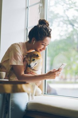 Öğrenci kullanarak Smartphone müzik zevk kulaklıkları kafede köpek okşayarak