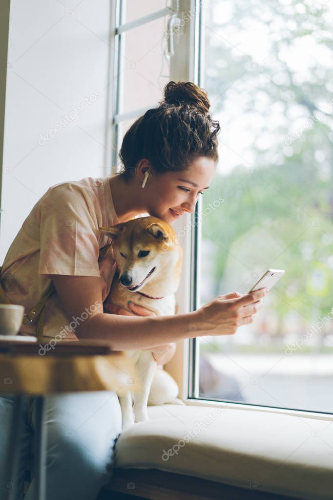 Student using smartphone enjoying music in earphones stroking dog in cafe