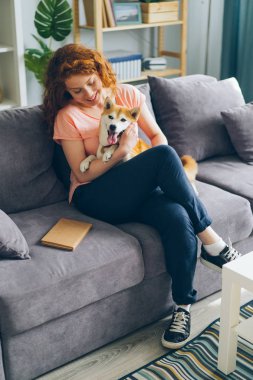 Mutlu genç kız sarılmak köpek oturma üzerinde kanepe üzerinde modern daire gülümseyen