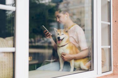 Bayan akıllı telefon kullanarak kablosuz kulaklıklar ile müzik dinleme köpek okşayarak