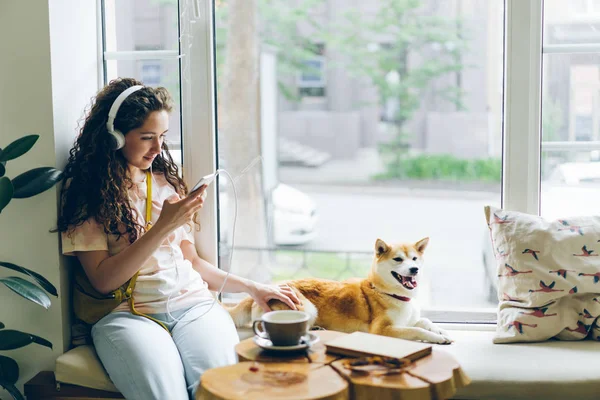 Hezká dívka naslouchající hudbě pomocí sluchátek smartphone, který sedí v kavárně — Stock fotografie
