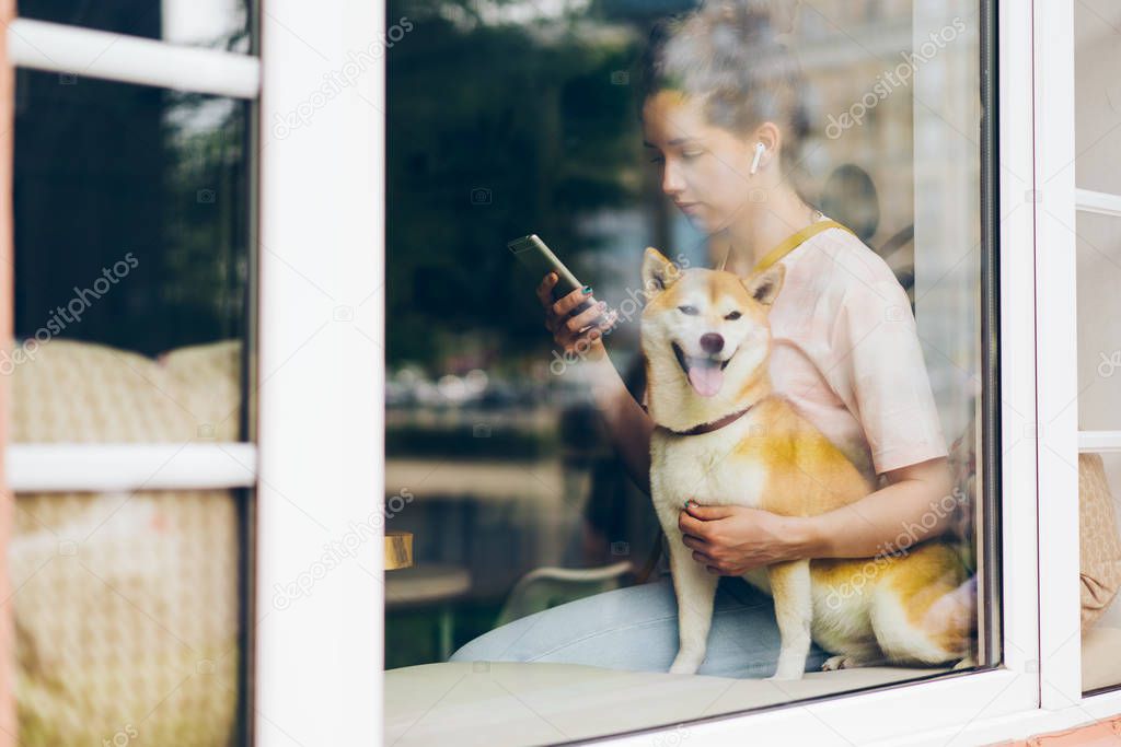 Girl using smartphone listening to music in wireless earphones with dog in cafe