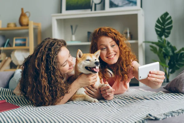 Hermanos tomando selfie con lindo cachorro acostado en el sofá en casa usando el teléfono inteligente —  Fotos de Stock