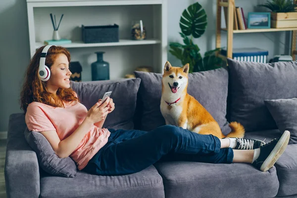 Student mit Kopfhörer hört Musik per Smartphone auf Couch mit Hund — Stockfoto