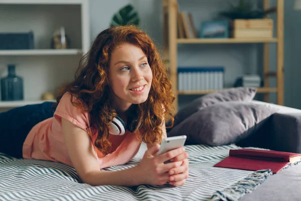 Portret van mooi meisje liggend op de Bank thuis houden smartphone glimlachend — Stockfoto