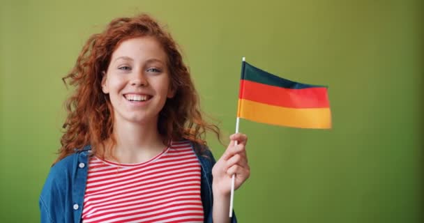 Piękna ruda dziewczyna trzyma niemiecką flagę uśmiechniętą na zielonym tle — Wideo stockowe