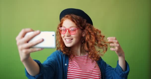 Портрет дівчини-підлітка, яка бере селфі зі смартфоном, махаючи рукою посміхаючись — стокове відео