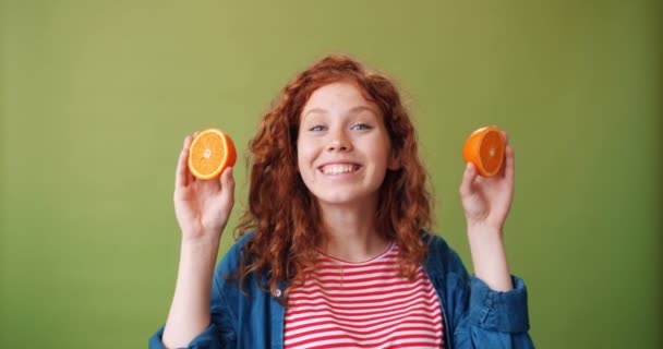 Csinos lány, aki friss narancsot tartott a szeme közelébe, mosolyogva, zöld alapon — Stock videók