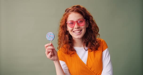 Gelukkig tiener meisje in zonnebril houdt Lollipop glimlachend op groene achtergrond — Stockvideo