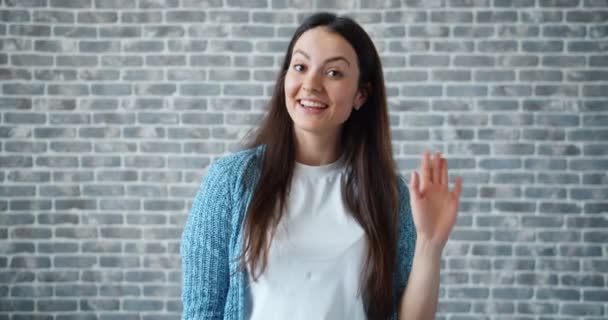 Porträt einer freundlichen Frau mit winkender Hand, die mit einem glücklichen Lächeln in die Kamera blickt — Stockvideo