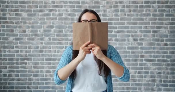 Fille heureuse dans des lunettes livre de lecture puis souriant sur fond de mur de briques — Video