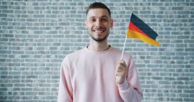 Alman bayrağı tutan ve tuğla duvar arka planda gülümseyen mutlu adam Portresi