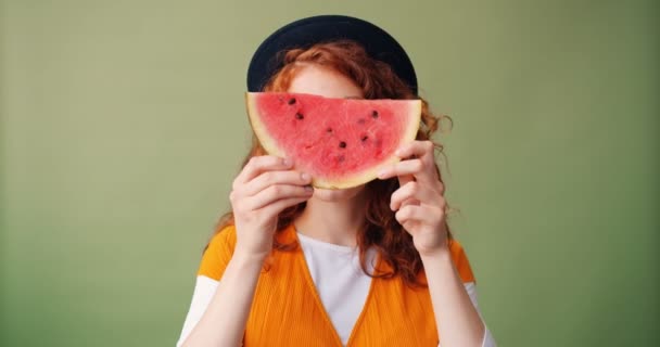 Portrait of girl holding watermelon smiling hiding face on green background — Stock Video