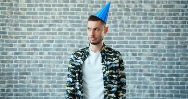 Portrait of unhappy young man taking off bright party hat looking at camera — Stock Video