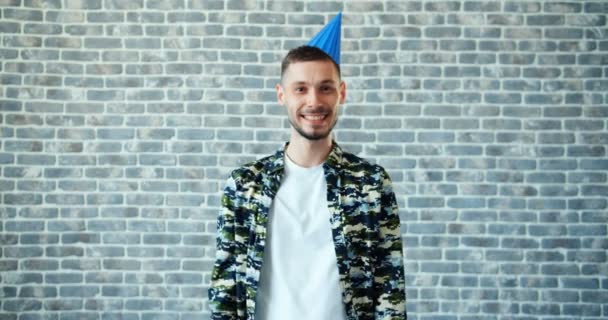Portret van de jonge man dragen verjaardag hoed wijzend op hoofd op bakstenen achtergrond — Stockvideo