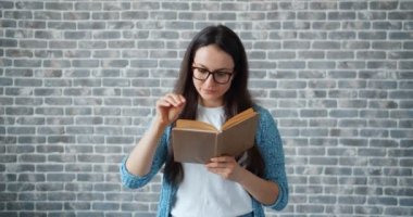 Gözlük ciddi kız tuğla duvar arka plan üzerinde kitap dönüm sayfası okuma