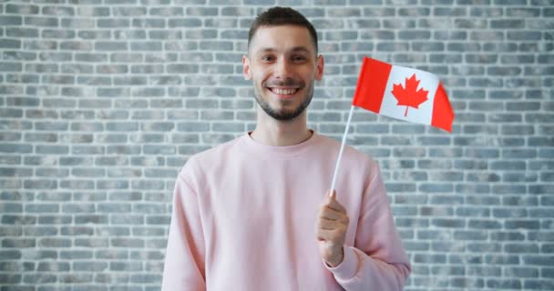 Retrato de estudante alegre segurando bandeira canadense no fundo da parede de tijolo — Vídeo de Stock