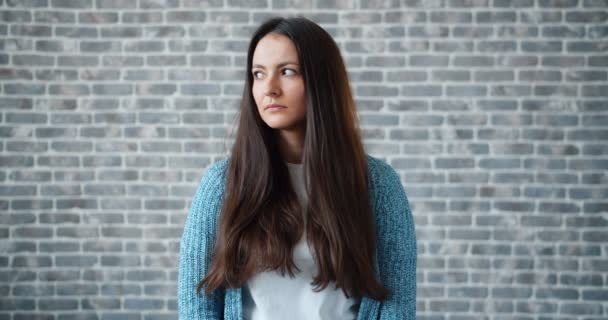 Portrait of sad young woman looking around then at camera on brick background — Stock Video