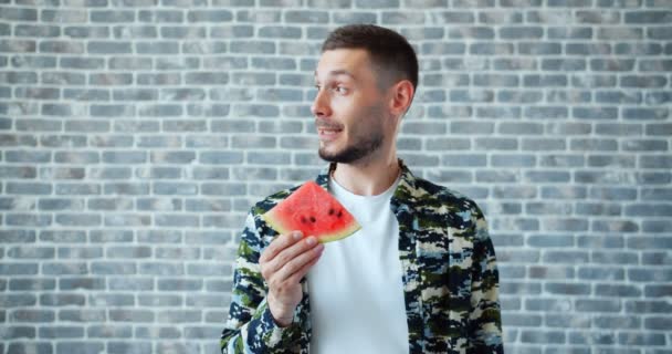 Retrato del hombre guapo comiendo melón de agua dulce sonriendo sobre fondo de ladrillo — Vídeo de stock