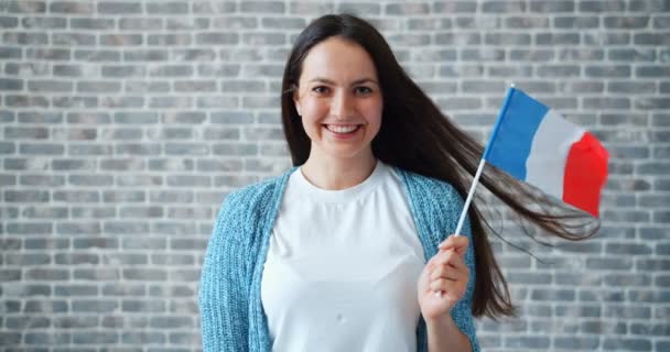 Retrato de bella dama sonriente sosteniendo bandera francesa sobre fondo de pared de ladrillo — Vídeos de Stock