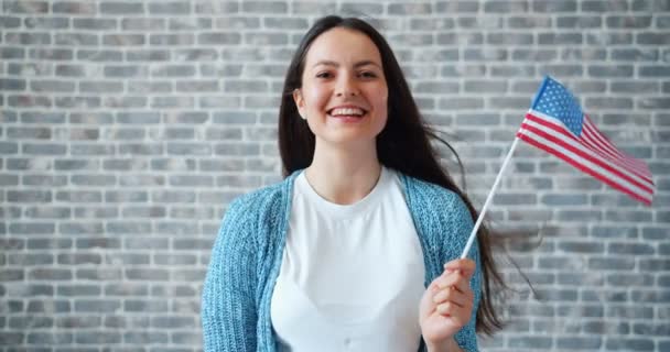 Portrait of cute girl holding American flag and smiling on brick wall background — Stock Video