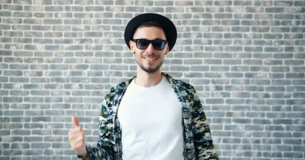 Portrait of man in hat and sunglasses dancing on brick wall background — Stok Video