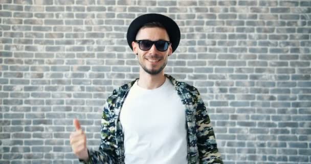 Retrato de hombre en sombrero y gafas de sol bailando sobre fondo de pared de ladrillo — Vídeo de stock