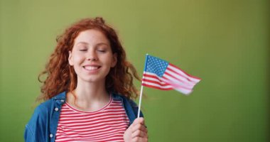 Yeşil arka planda Amerikan bayrağı tutan çekici kızıl saçlı genç