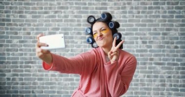 Akıllı telefon ile selfie çekerken saç silindirleri ve göz yamaları ile neşeli kız