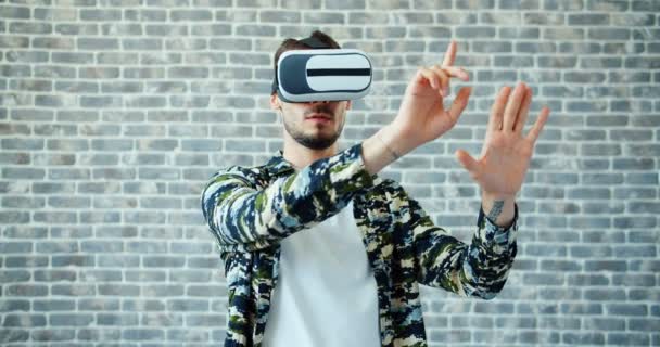 Retrato del hombre usando gafas de realidad virtual moviendo las manos sobre el fondo de ladrillo — Vídeos de Stock
